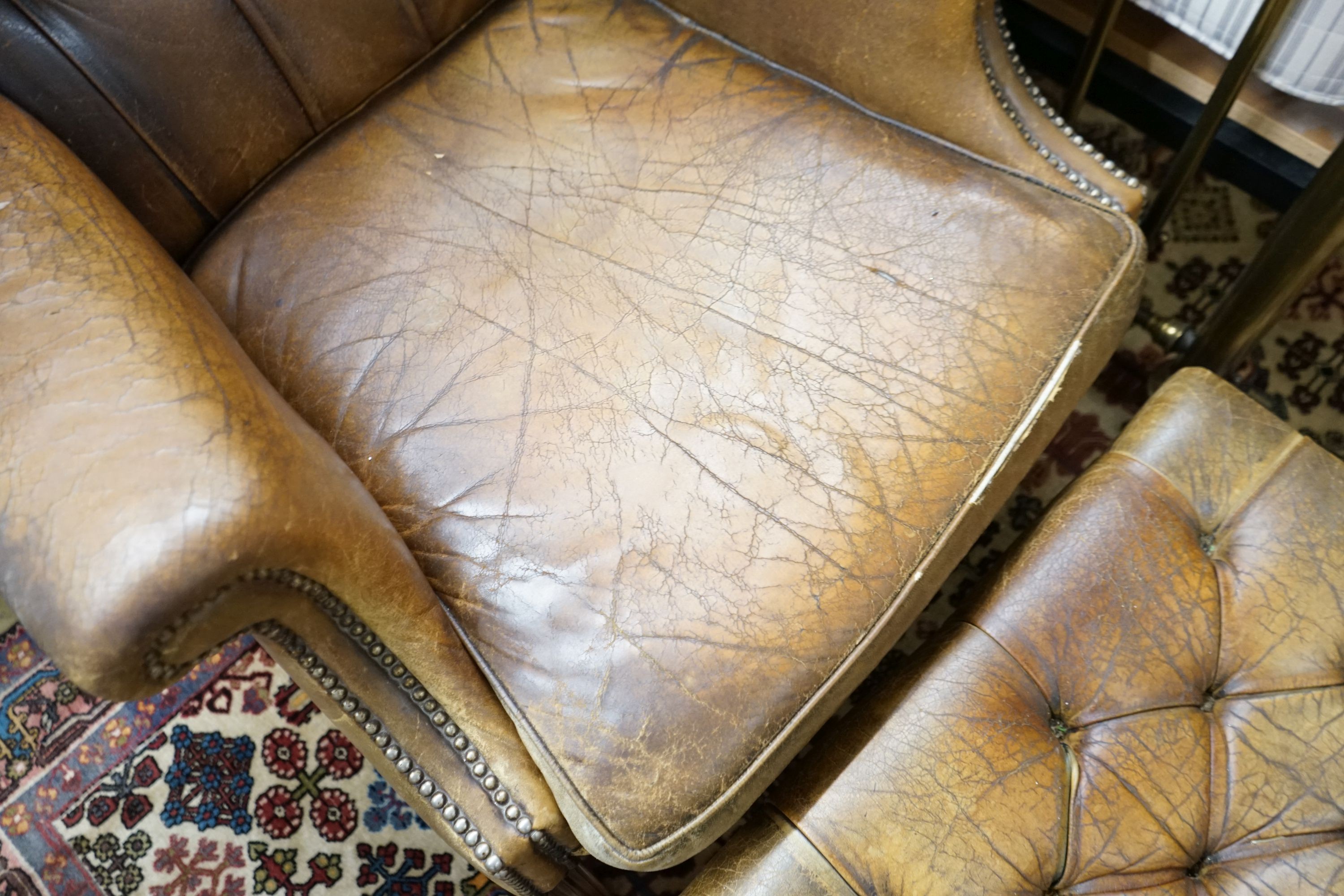 A leather wing armchair upholstered in buttoned brown leather, width 82cm, depth 77cm, height 110cm together with a similar foot stool